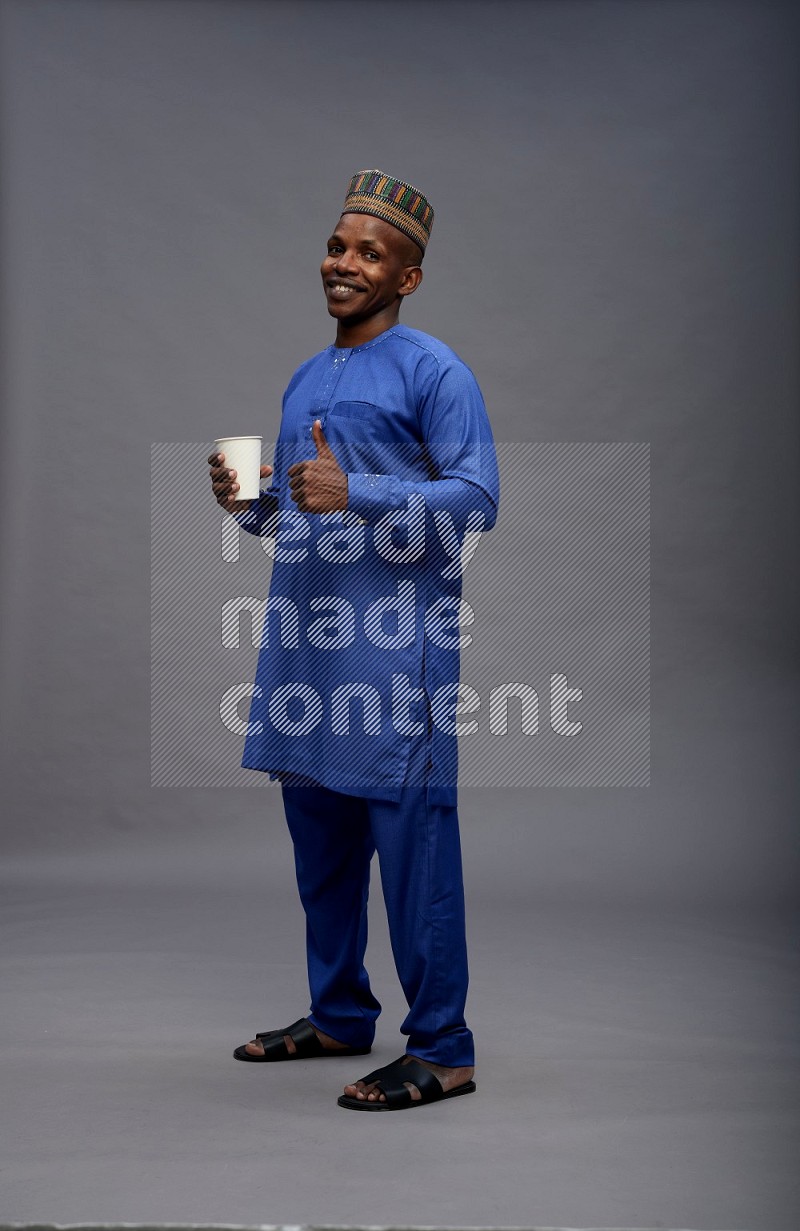 Man wearing Nigerian outfit standing holding paper cup on gray background