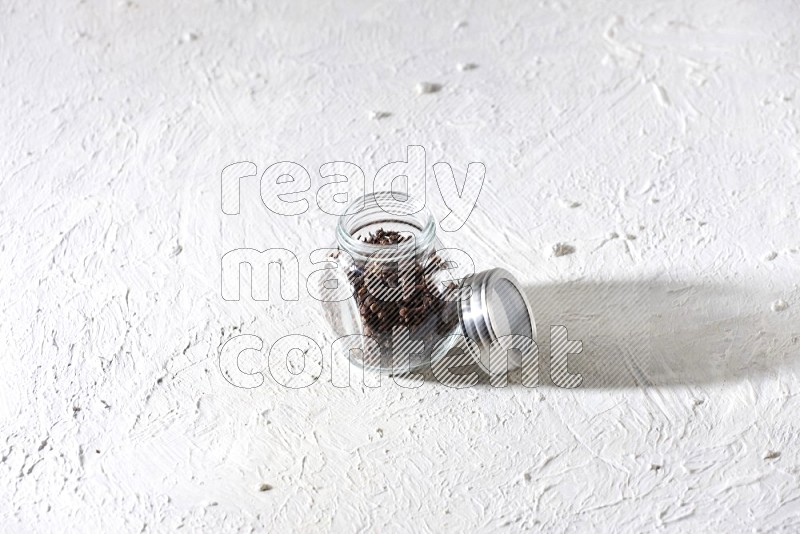 A glass spice jar full of cloves on textured white flooring