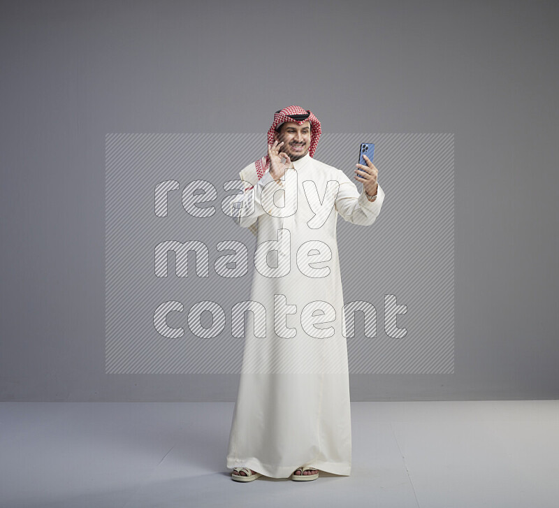 رجل سعودي يرتدي ثوب ابيض وشماغ احمر يقوم بمحادثه فيديو باستخدام جواله