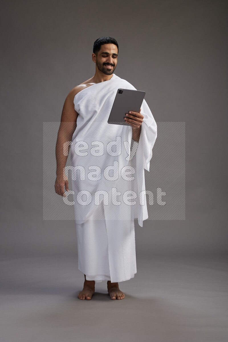 A man wearing Ehram and holding a tablet on gray background