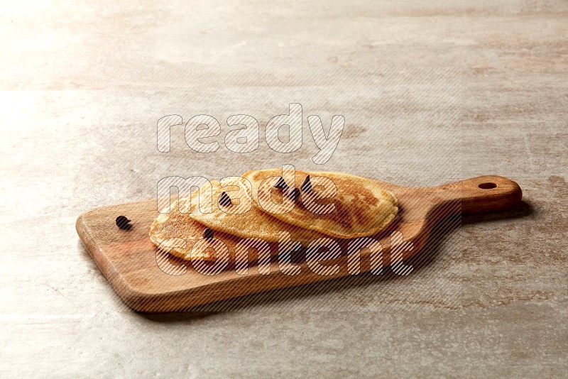 Three stacked chocolate chips pancakes on a wooden board on beige background