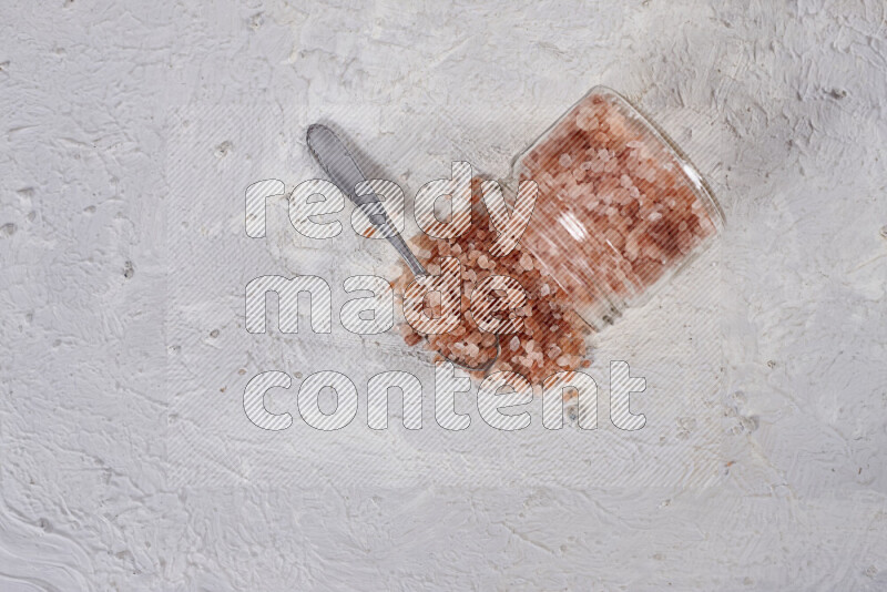 A glass jar full of coarse himalayan salt crystals on white background