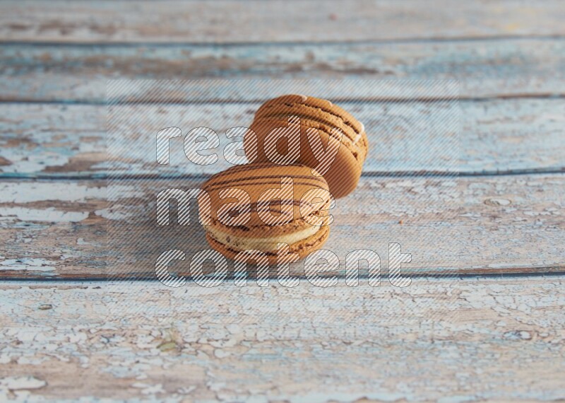45º Shot of of two assorted Brown Irish Cream, and light brown Almond Cream macarons next to each other on light blue background
