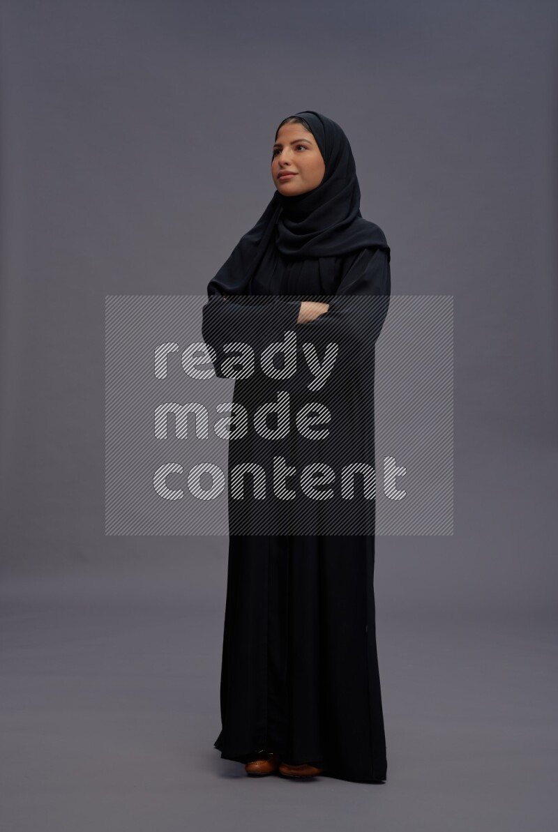 Saudi woman wearing Abaya standing with crossed arms on gray background
