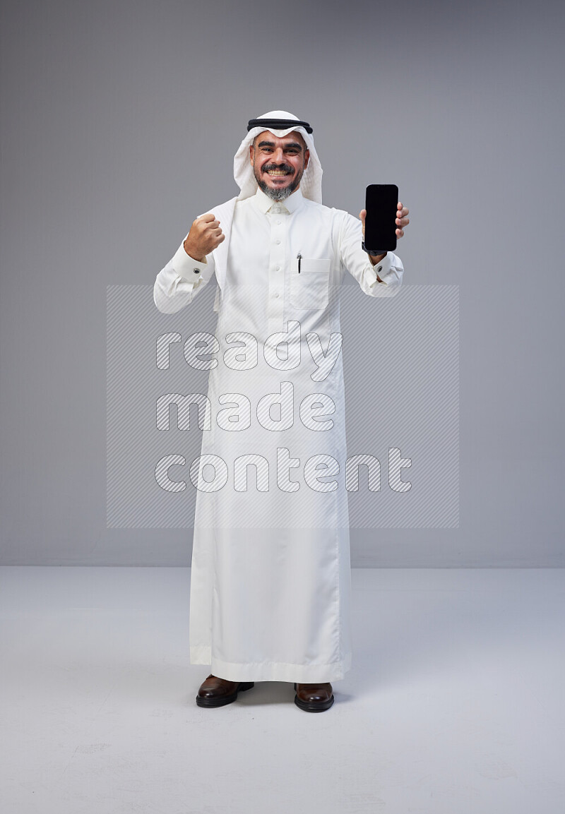 رجل سعودي يرتدي ثوب وشماغ ابيض يحمل جوال