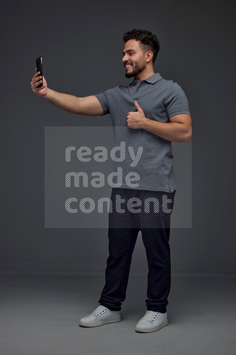 A man wearing casual and taking selfie with his phone different angles eye level on a gray background