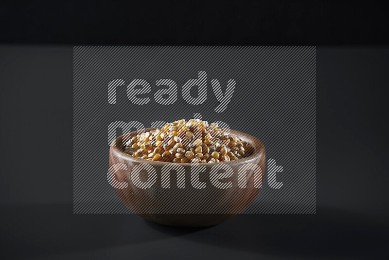 Dry corn kernels in a wooden bowl on grey background