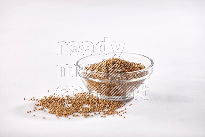 A glass bowl full of mustard seeds and more seeds spread on a white flooring in different angles