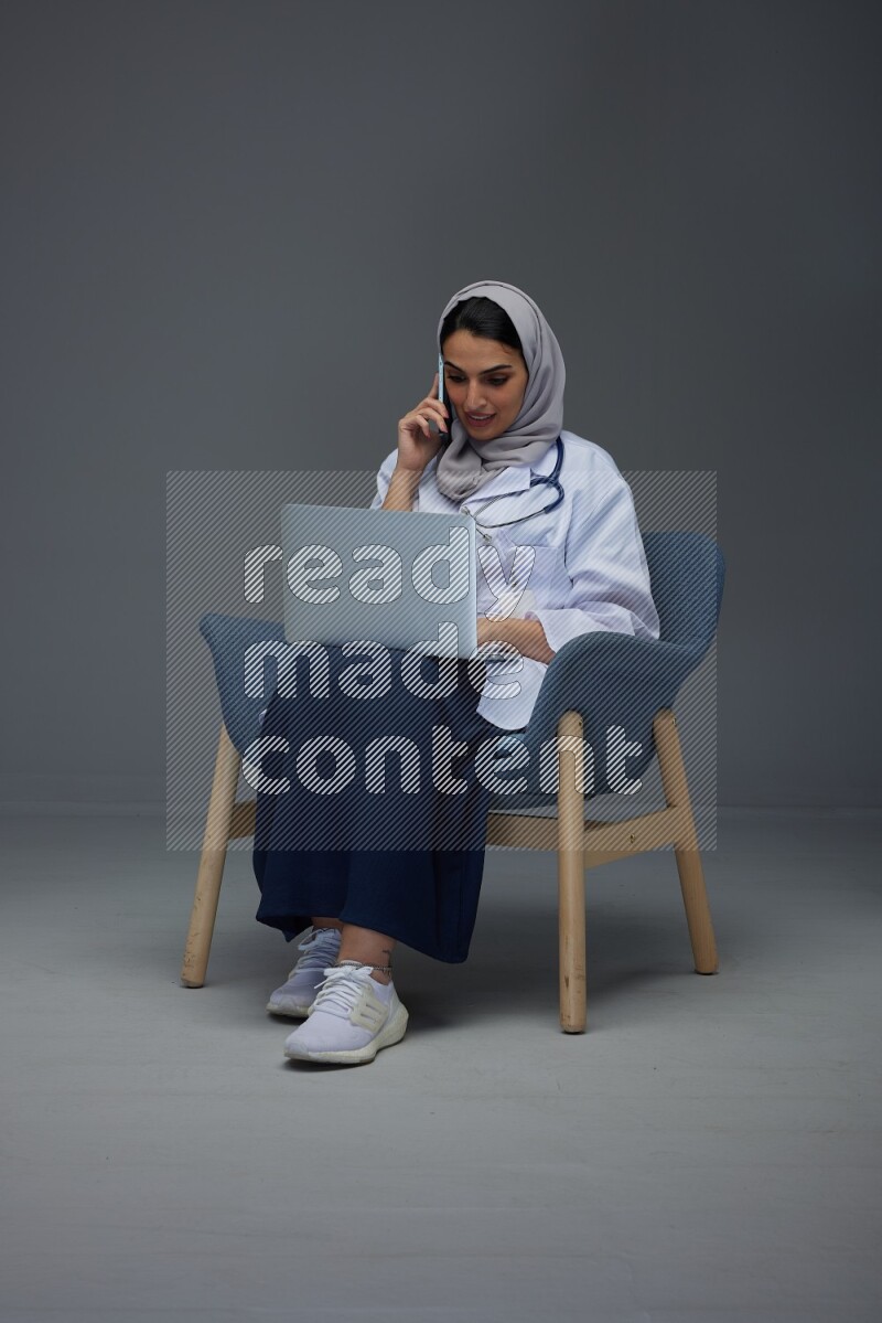 A doctor wearing a light gray head scarf sitting on blue chair on grey background