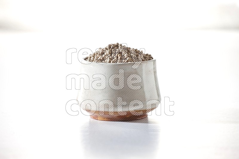 A beige pottery bowl full of white pepper beads on white flooring