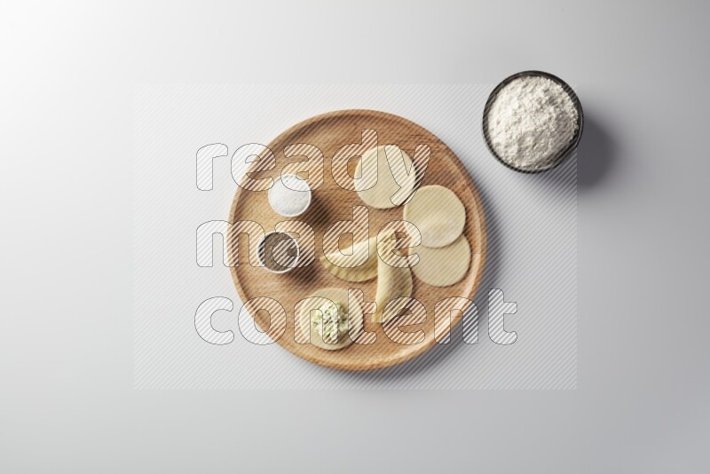 two closed sambosas and one open sambosa filled with cheese while flour, salt, and black pepper aside in a wooden dish on a white background