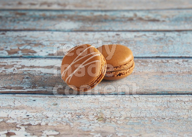 45º Shot of of two assorted Brown Irish Cream, and Brown Maple Taffy macarons  on light blue background