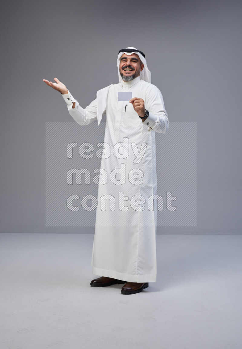 Saudi man Wearing Thob and white Shomag standing holding ATM card on Gray background