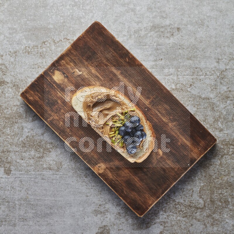 open faced peanut butter sandwich with blueberries and pistachio on a grey textured background