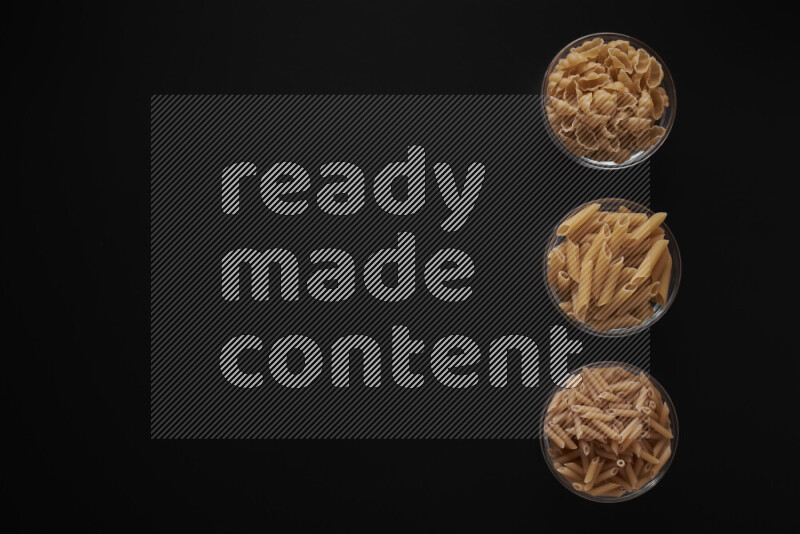 Different pasta types in 3 glass bowls on black background