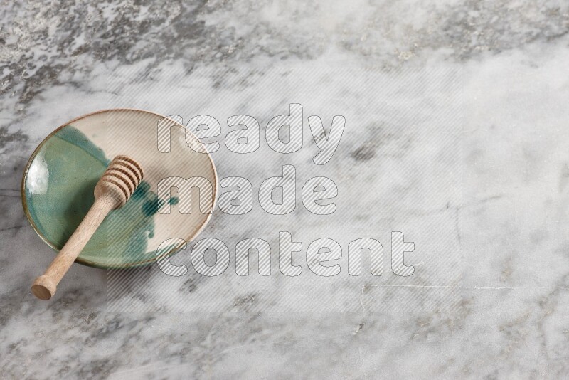 Multicolored pottery plate with wooden honey dipper in it on grey marble background