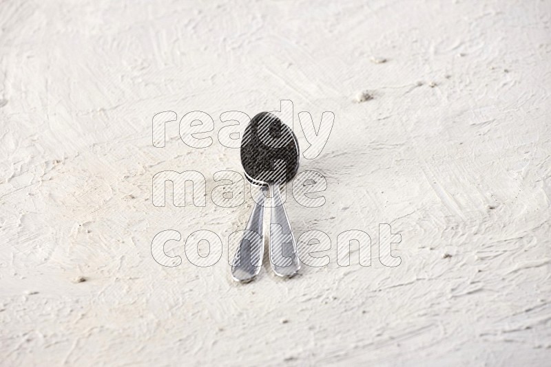 2 metal spoons full of black seeds on textured white flooring