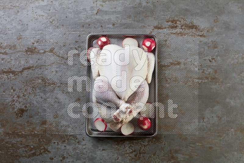 whole Raw chicken on a small oven trey direct on a rustic grey background