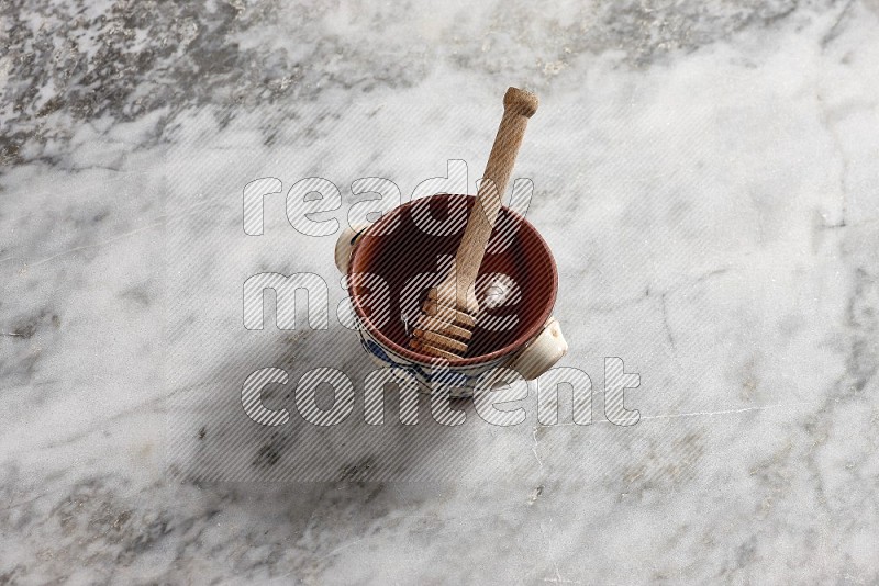 Decorative Pottery Pot with wooden honey handle in it, on grey marble flooring, 65 degree angle