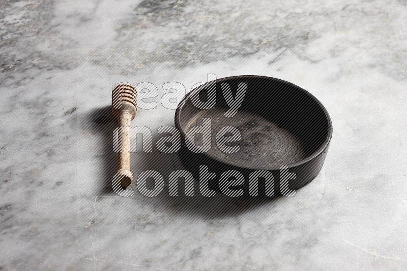 Black Pottery Oven Plate with wooden honey handle on the side with grey marble flooring, 45 degree angle