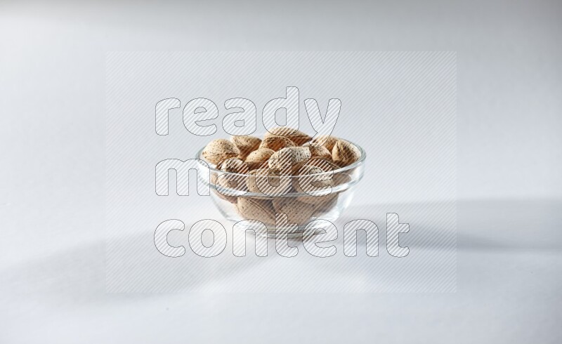 A glass bowl full of almonds on a white background in different angles