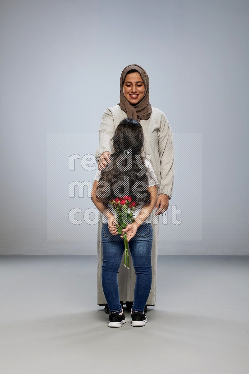 A girl hiding a flower behind her back for her mother on gray background