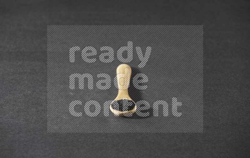 A wooden spoon full of black seeds on a black flooring