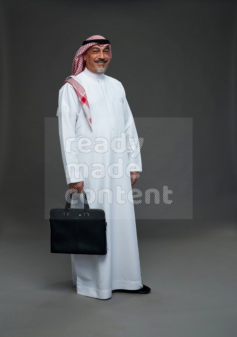 Saudi man with shomag Standing holding bag on gray background