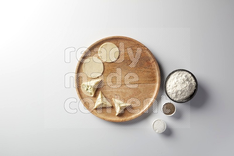 two closed sambosas and one open sambosa filled with cheese while flour, salt, and black pepper aside in a wooden dish on a white background