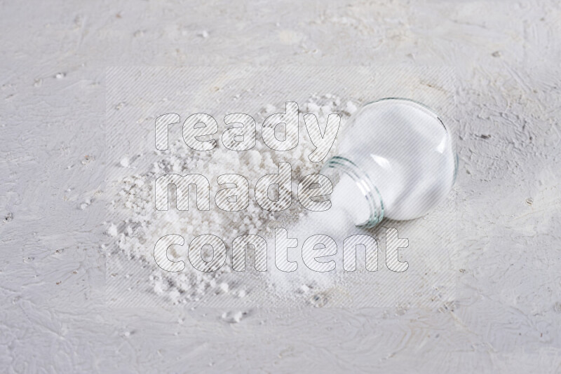 A glass jar full of table salt with some sea salt crystals beside it on a white background