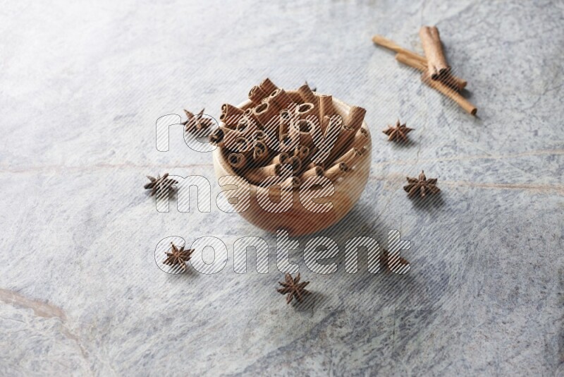 wooden bowl full of cinnamon sticks surrounded by star anis on marble background in different angles