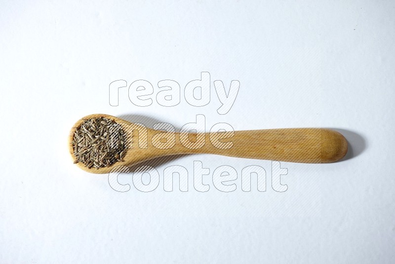 A wooden spoon full of cumin seeds on a white flooring