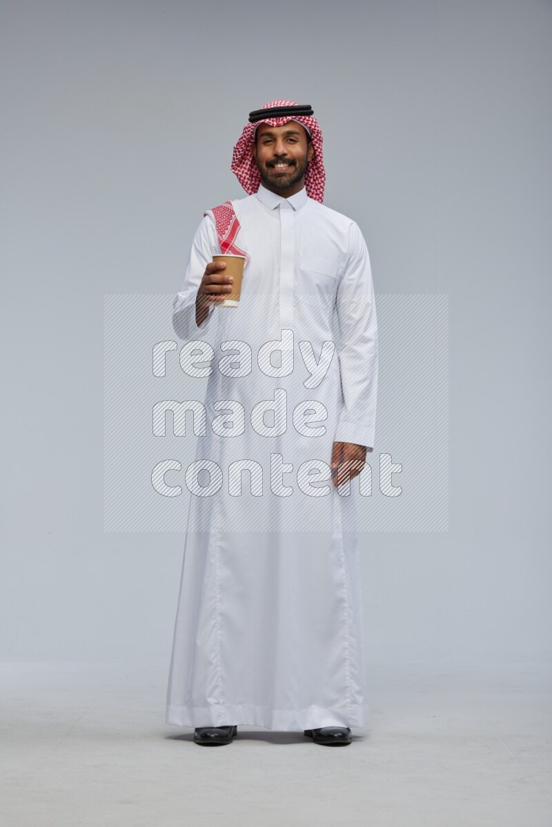 Saudi man Wearing Thob and shomag standing holding paper cup on Gray background