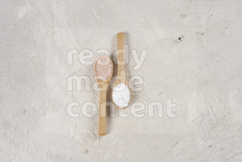 2 wooden spoons filled with fine and coarse salt on white background