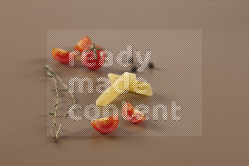 Raw pasta with different ingredients such as cherry tomatoes, garlic, onions, red chilis, black pepper, white pepper, bay laurel leaves, rosemary and cardamom on beige background