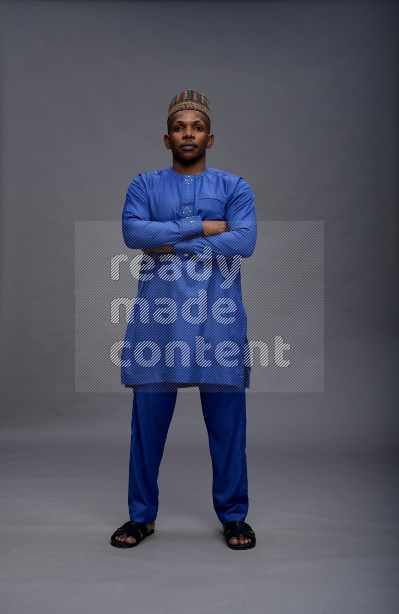Man wearing Nigerian outfit standing with crossed arms on gray background