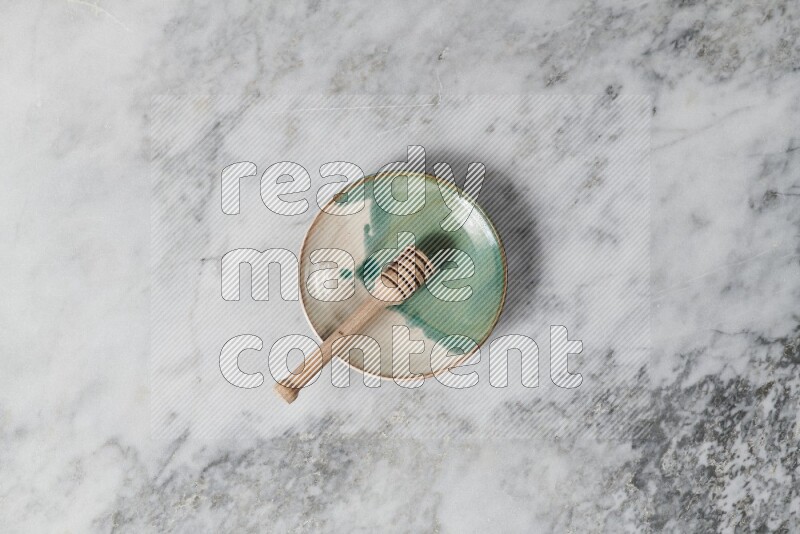 Multicolored pottery plate with wooden honey dipper in it on grey marble background
