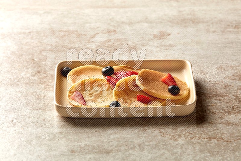 Five stacked mixed berries mini pancakes in a rectangular plate on beige background