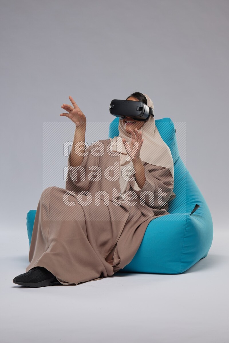 A Saudi woman sitting on a blue beanbag and gaming with VR