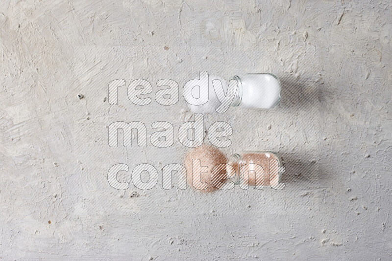 2 glass jars one is full of fine himalayan salt and the other with table salt on white background