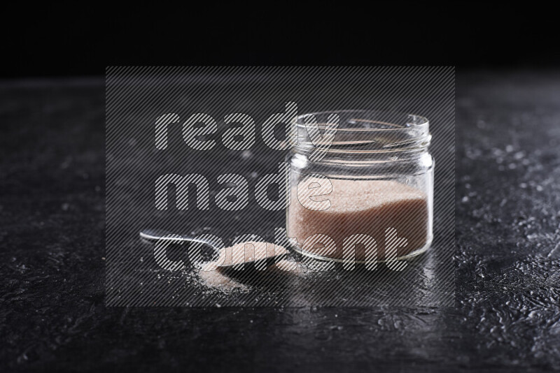 A glass jar full of fine himalayan salt on black background