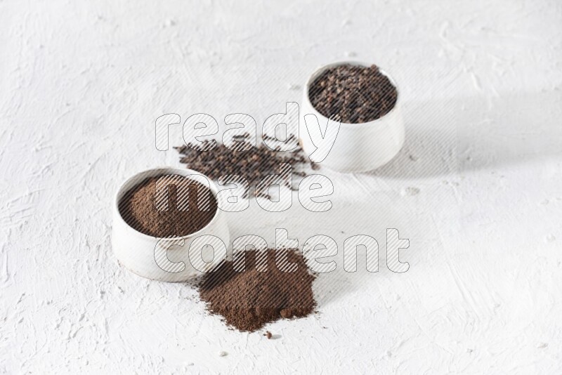 2 Beige ceramic bowls, one full of cloves and the other full of powder on textured white flooring