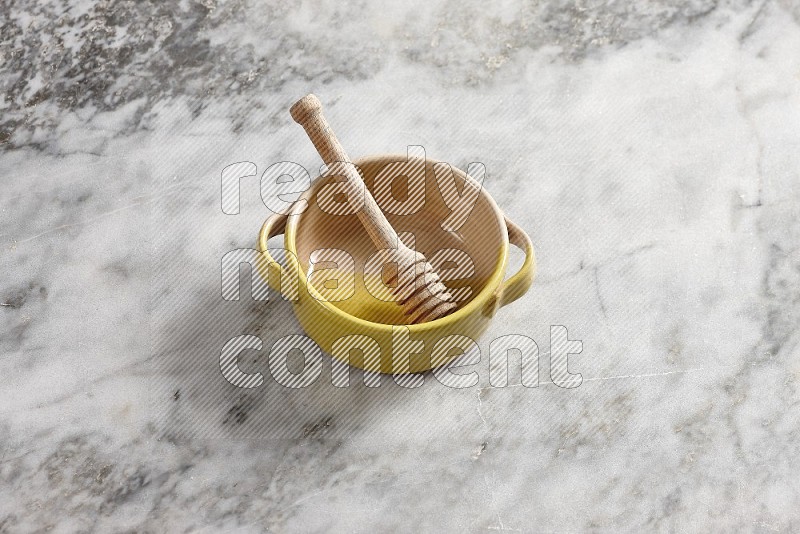 Multicolored Pottery bowl with wooden honey handle in it, on grey marble flooring, 65 degree angle