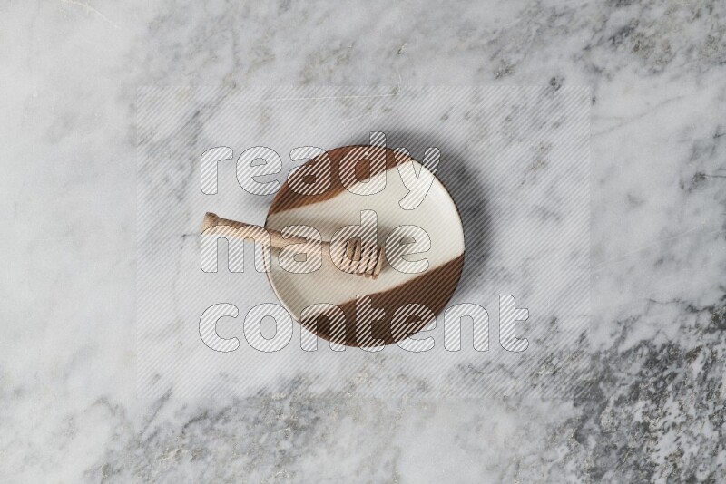 Multicolored pottery plate with wooden honey dipper in it on grey marble background