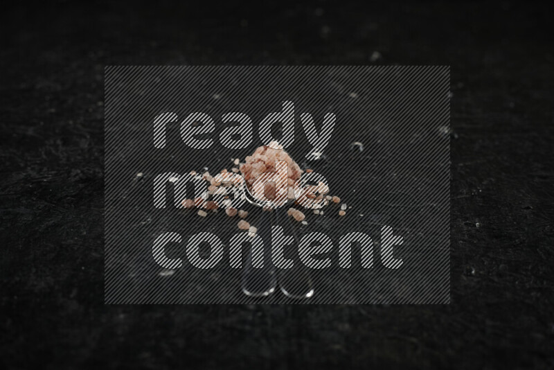 2 metal spoons filled with pink himalayan salt on black background