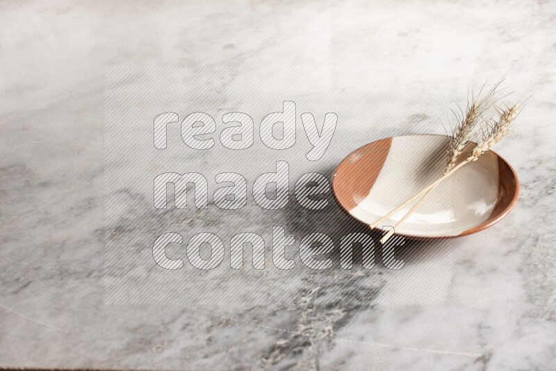 Wheat stalks on multicolored pottery plate on grey marble background