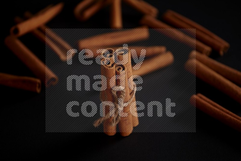 4 Cinnamon sticks stacked and bounded with more sticks in the background on black flooring