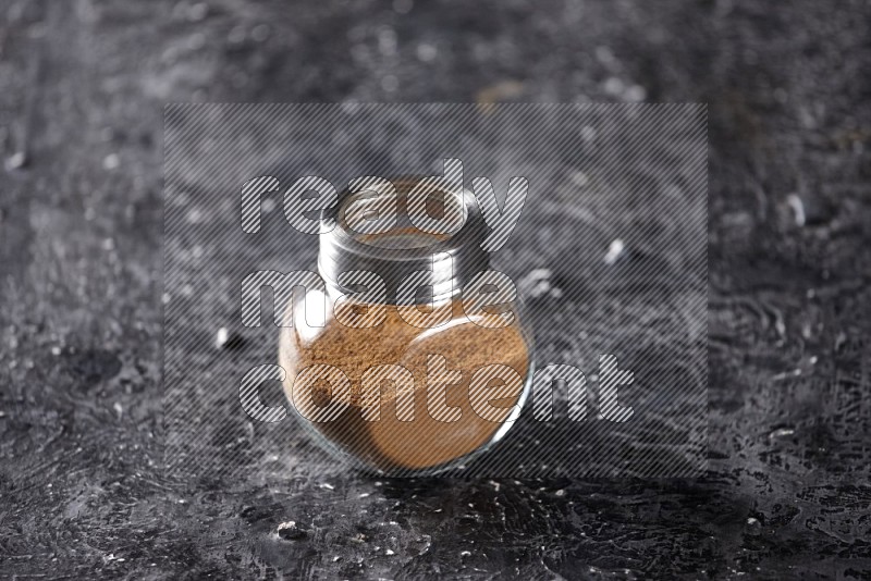 Herbal glass jar full of cinnamon powder on a textured black background