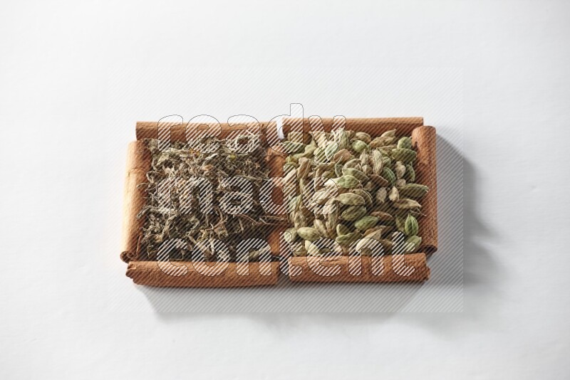 مربعان من أعواد القرفة ممتلئان بحبوب الهيل والريحان المجفف علي خلفية بيضاء