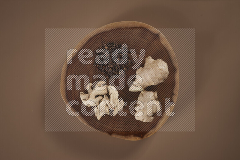 An assorted whole spices on a flat wooden tray including fresh and dried ginger, cinnamon sticks, cardamom, turmeric fingers, cloves, star anise on beige background